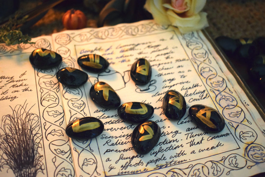 Black runes with gold symbols spilled out onto an open page of a grimoire with herbs, flowers and crystals in the background