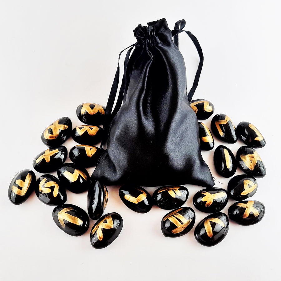 Black runes with gold symbols spilled out around a black satin drawstring pouch