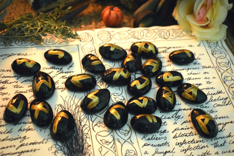 Black runes with gold symbols spilled out onto an open page of a grimoire with herbs, flowers and crystals in the background