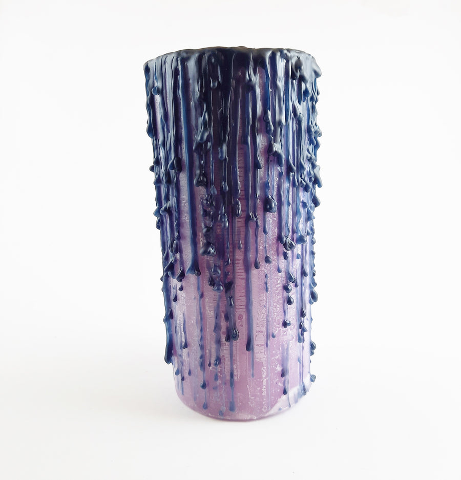 A purple pillar candle with black drips with a white background