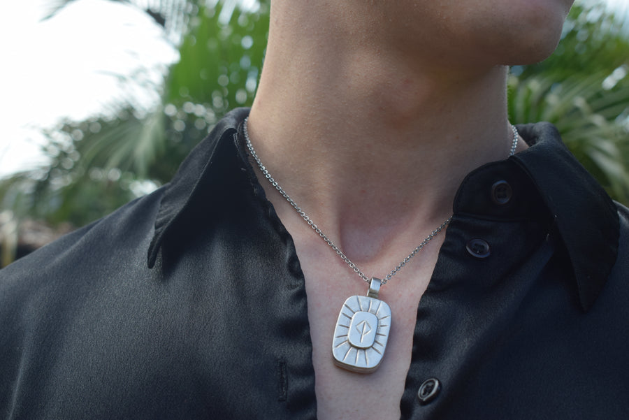 Person's neck with open shirt showing handmade sterling silver pendant on chain inscribed with rune of protection