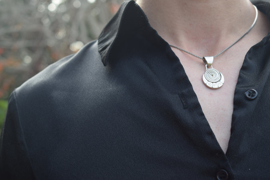 Chest with black shirt revealing a sterling silver spiral and runic necklace and chain