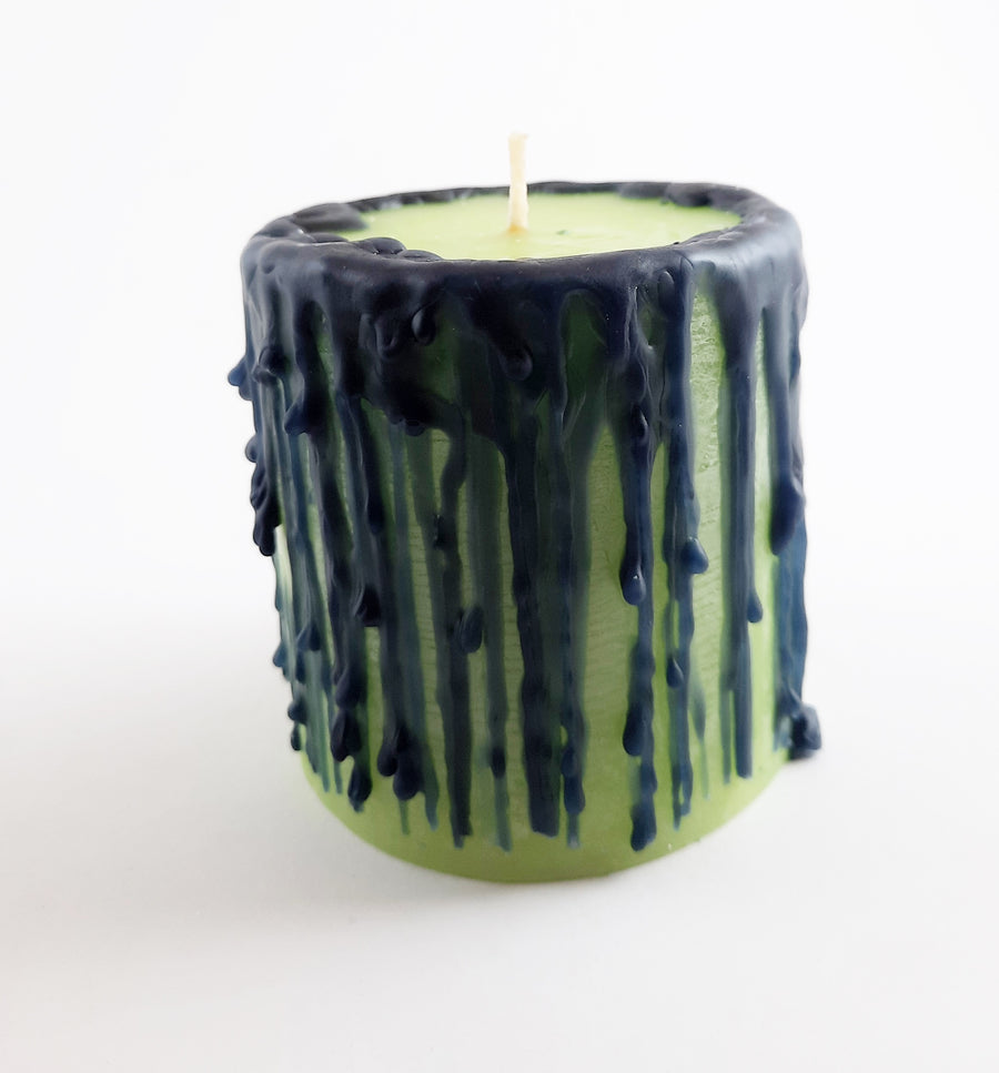 A green pillar candle with black drips sits on a white background