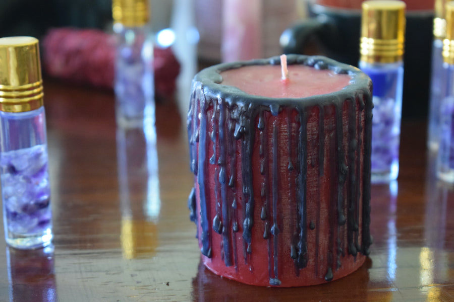 A red candle with black drips sits with crystal vials in the background.