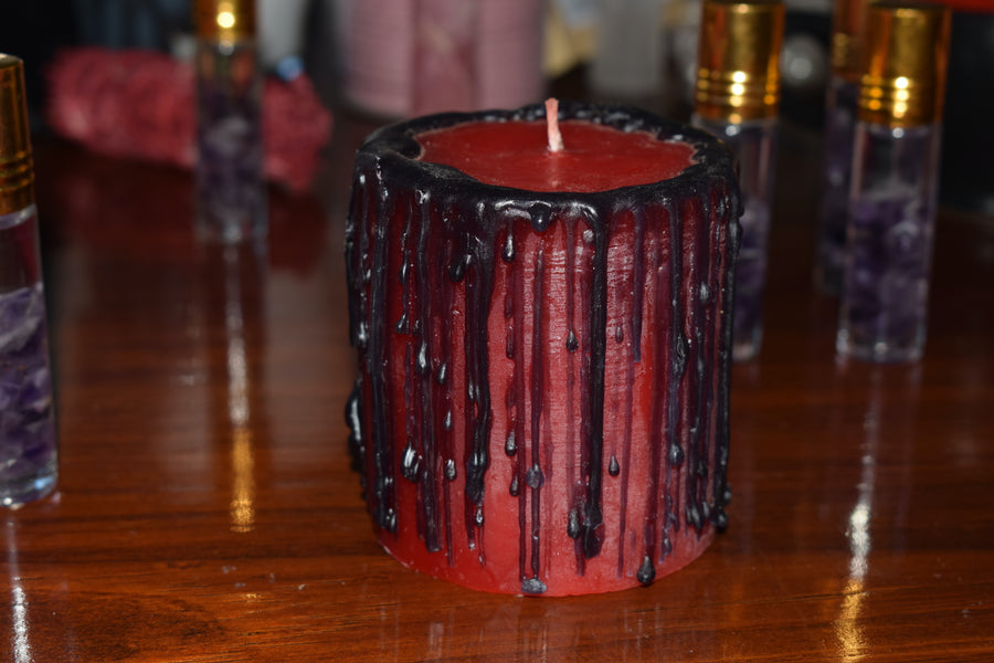 A red candle with black drips sits with crystal vials in the background.