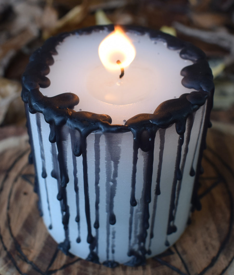 A black and white pillar candle with a flame licking from its wick rests on a wooden pentagram disk 