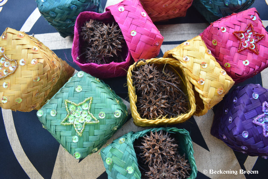 A pile colourful raffia boxes containing witches burrs resting on a pentagram altar cloth