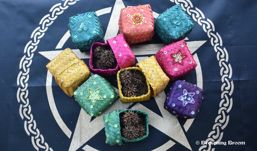 Ten colourful raffia boxes containing witches burrs resting on a pentagram altar cloth