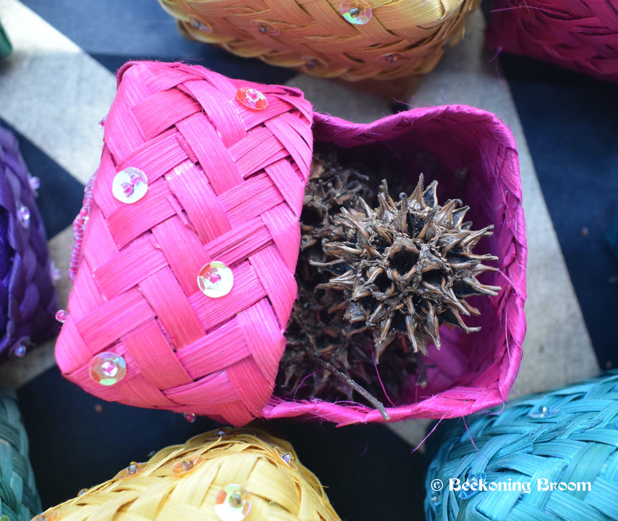 Pink raffia boxes containing witches burrs resting on a pentagram altar cloth
