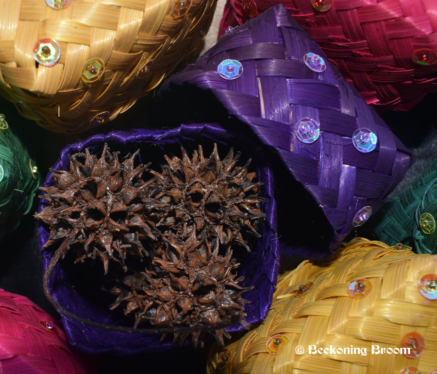 Purple raffia boxes containing witches burrs resting on a pentagram altar cloth