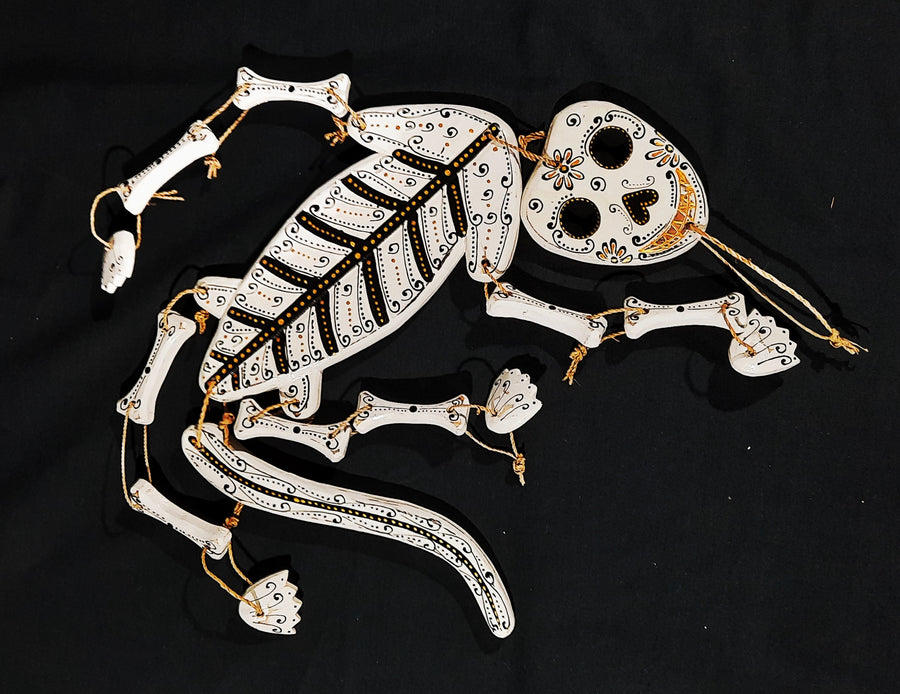 A white lizard skeleton calavera spirit rattle with gold and black lying on a black background 