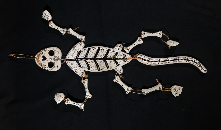 A white lizard skeleton calavera medicine rattle with gold and black lying on a black background 