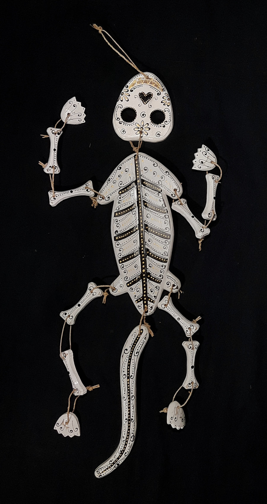 A white lizard skeleton calavera spirit medicine rattle with gold and black lying on a black background 