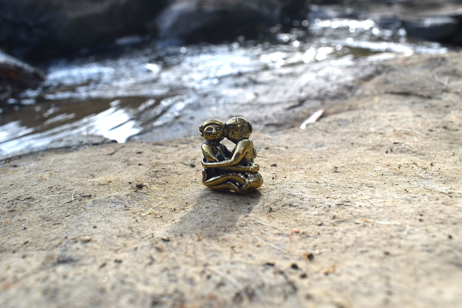 Small solid bronze ornament of lovers embracing each other resting on earth with creek in background