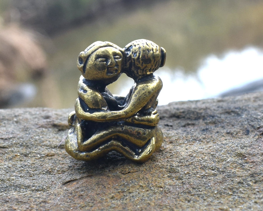Small solid bronze ornament of lovers embracing each other resting on a rock with creek in background
