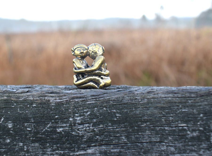 Small solid bronze ornament of lovers embracing each other resting on weathered timber fence paling with mountains in background