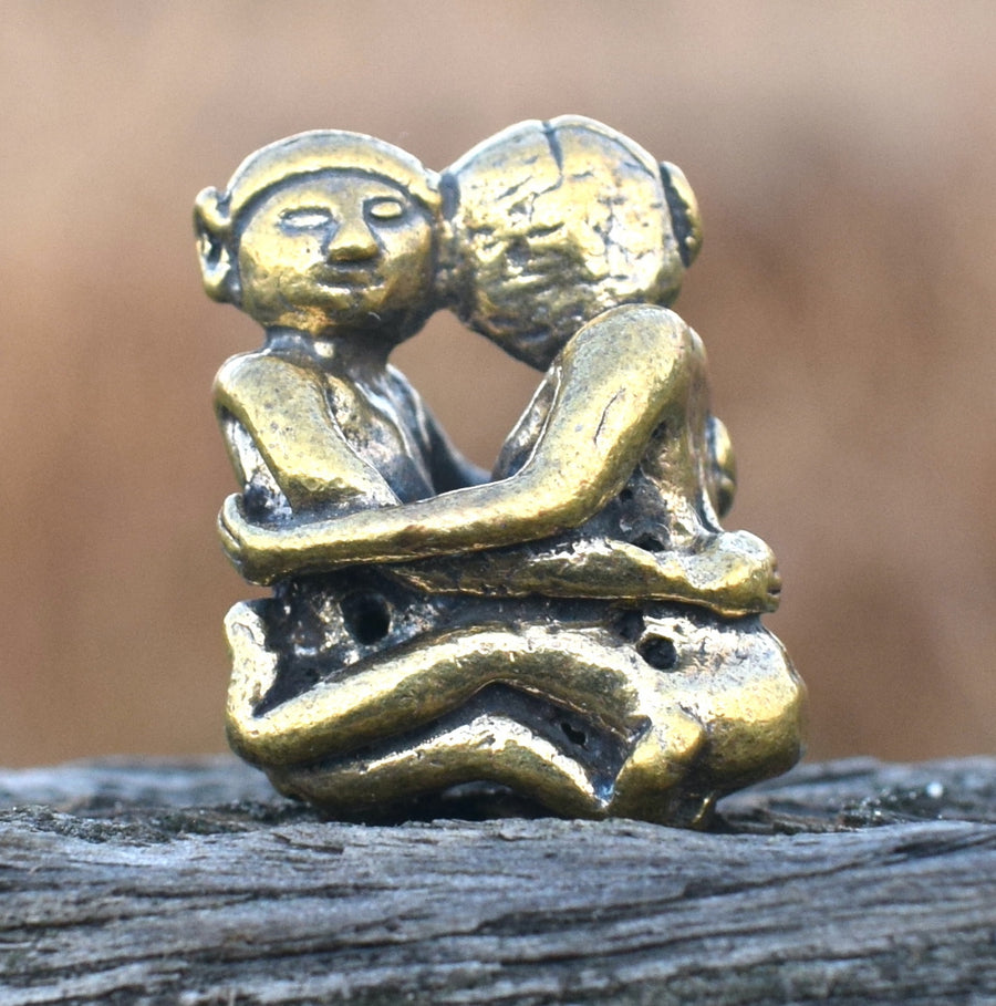 Small solid bronze ornament of lovers embracing each other resting on weathered timber