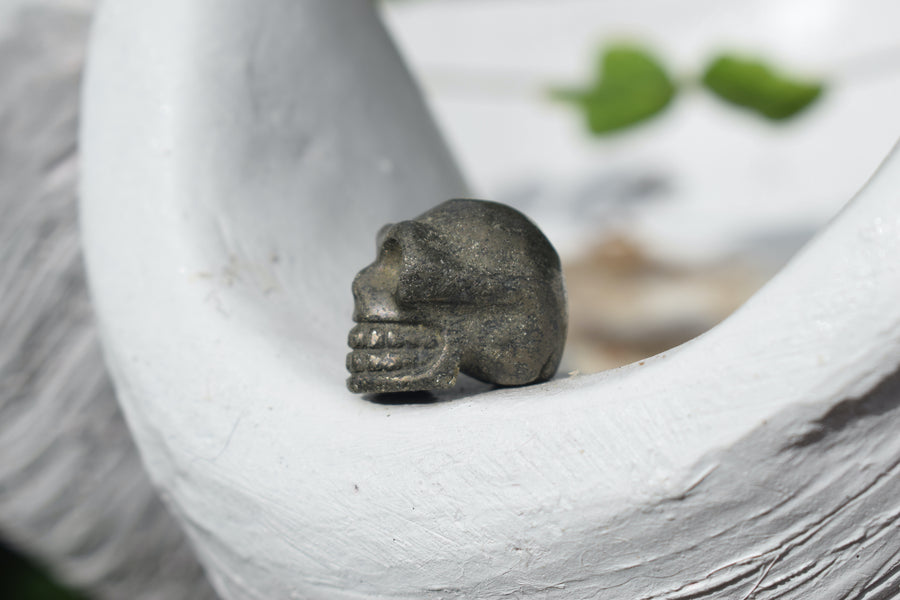 A mini skull carved from gold pyrite rests on a white shell.