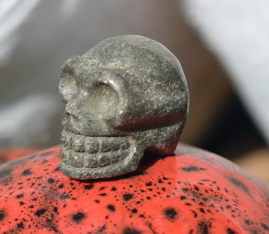 A mini human skull carved from gold pyrite sits on a ceramic mushroom.