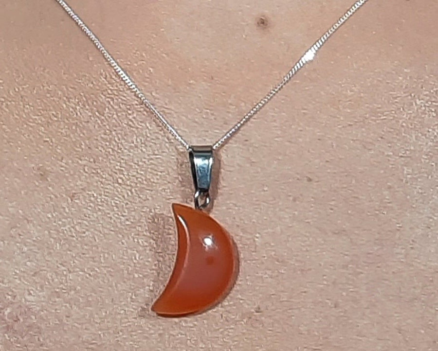 A carnelian crystal crescent moon necklace on a sterling silver chain hanging on the neck of a person