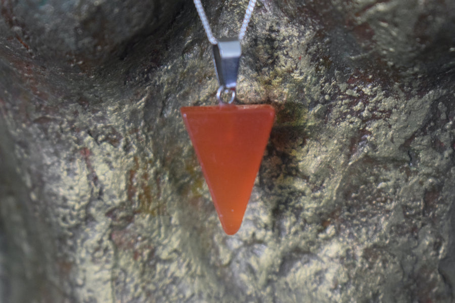 An orange carnelian crystal inverted triangle necklace on a sterling silver chain hanging on the neck of a bronze sculpture