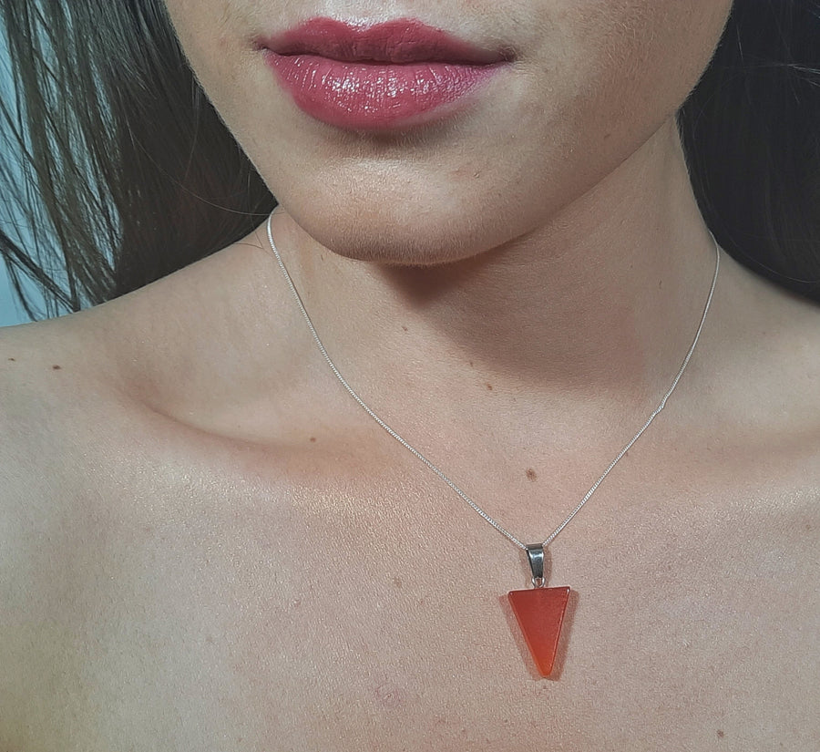 An orange carnelian crystal inverted triangle necklace on a sterling silver chain hanging on the neck of a person