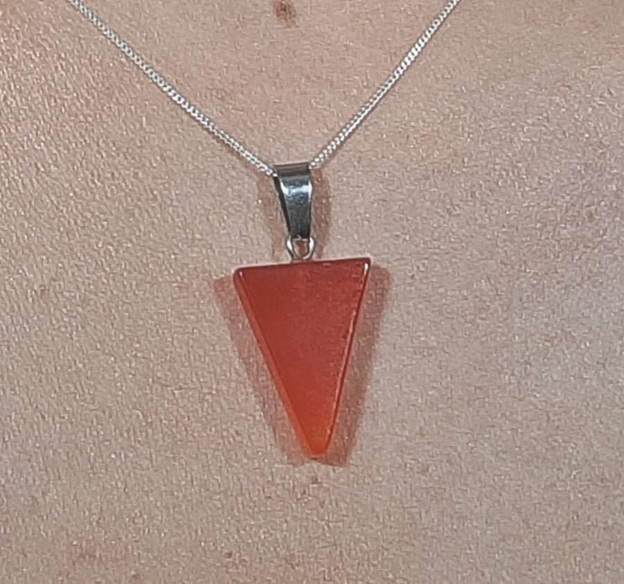 An orange carnelian crystal inverted triangle necklace on a sterling silver chain hanging on the neck of a person