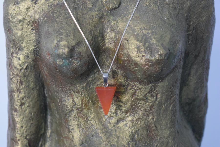An orange carnelian crystal inverted triangle necklace on a sterling silver chain hanging on the neck of a bronze goddess sculpture