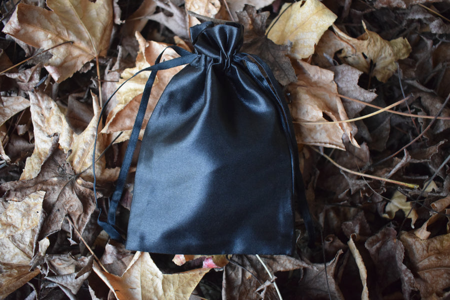 A black satin fabric drawstring pouch nestled on a bed of autumn leaves.