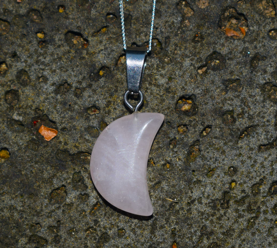 Rose quartz crescent moon pendant on silver chain resting on stone