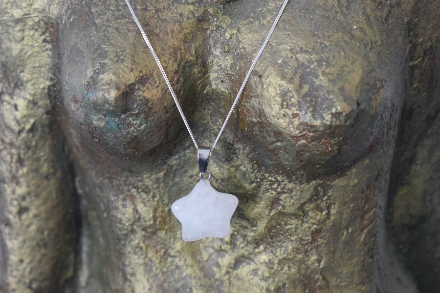 A rose quartz crystal pentagram star necklace on a sterling silver chain hanging on the neck of a bronze goddess sculpture