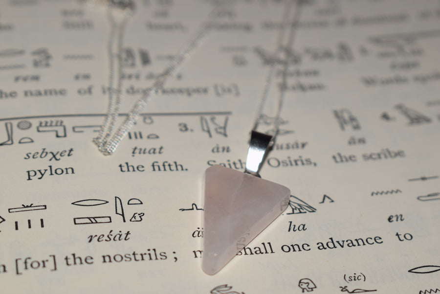 Rose quartz crystal triangle trinity pendant on sterling silver chain resting on Egyptian hieroglyphs parchment