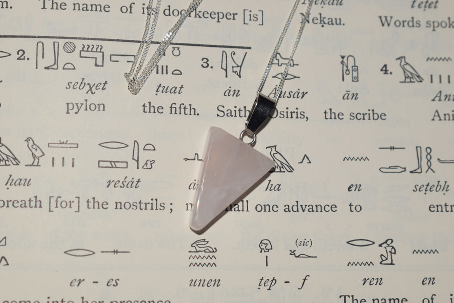 Rose quartz crystal triangle trinity pendant on sterling silver chain resting on Egyptian hieroglyphs parchment