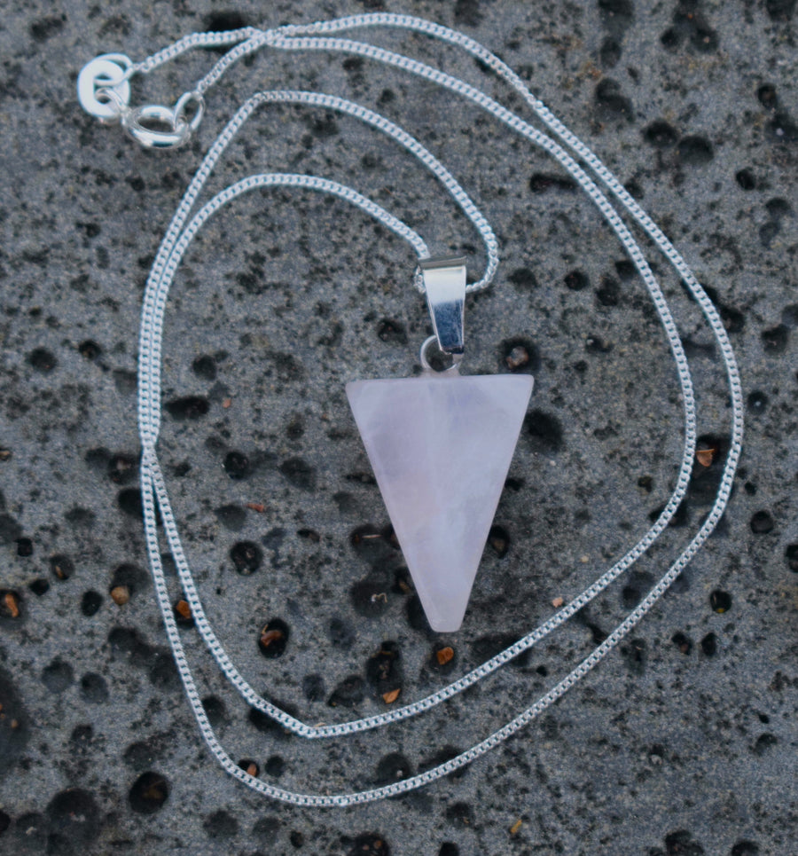 Rose quartz crystal triangle trinity pendant on sterling silver chain resting on a gray rock