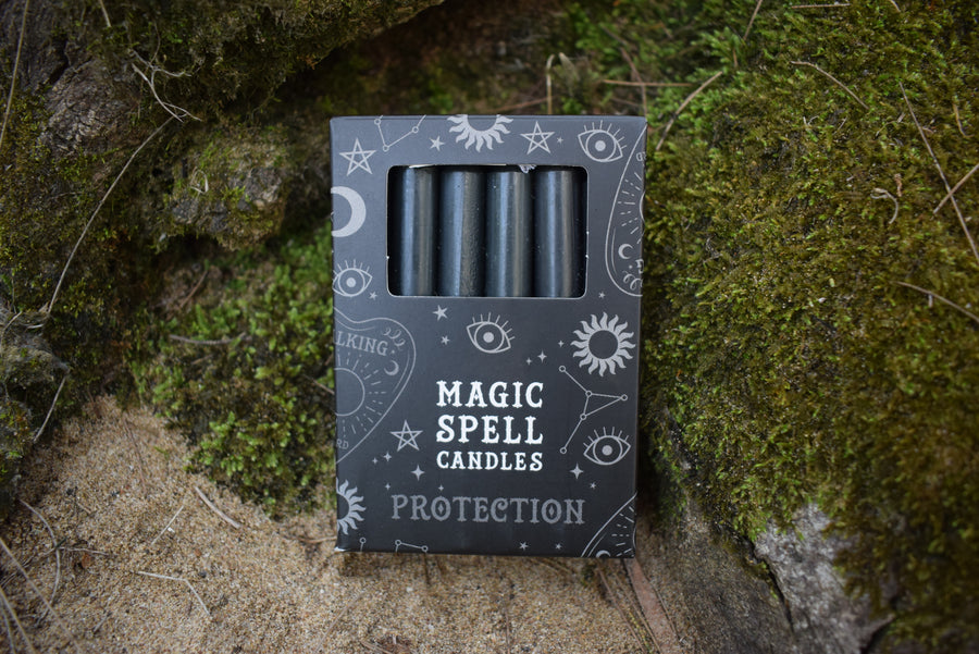 A packet of 12 taper candles in a box with Magic Spell Candles Protection written on the box. They rest on a mossy log.