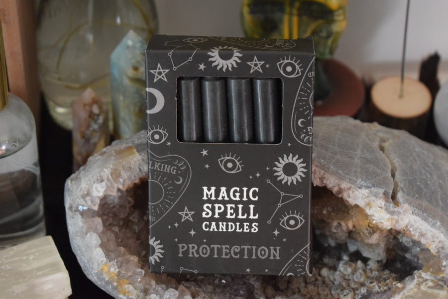 A packet of 12 taper candles in a box with Magic Spell Candles Protection written on the box. They rest on a crystal geode.