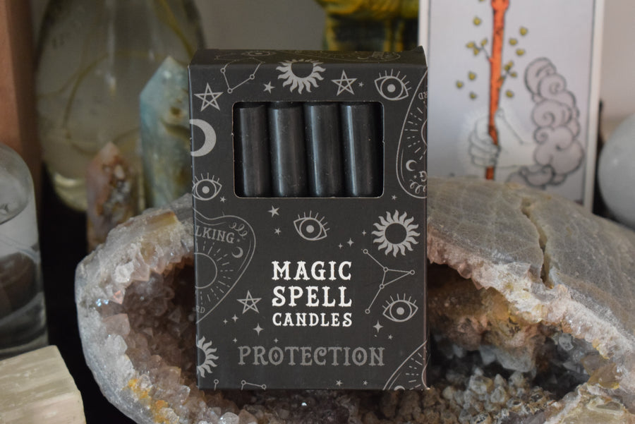 A packet of 12 taper candles in a box with Magic Spell Candles Protection written on the box. They rest on crystal geode.