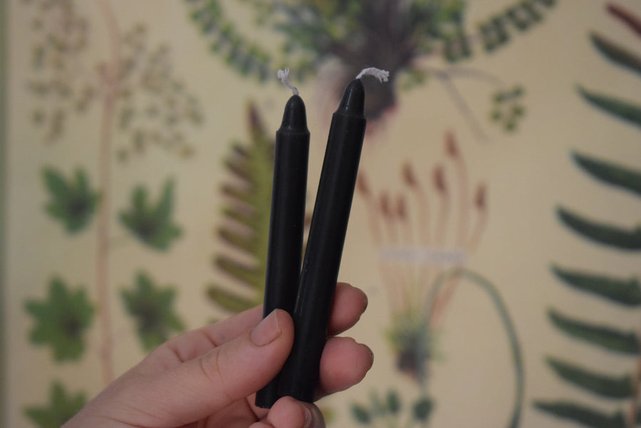 A hand holds two small black taper candles.
