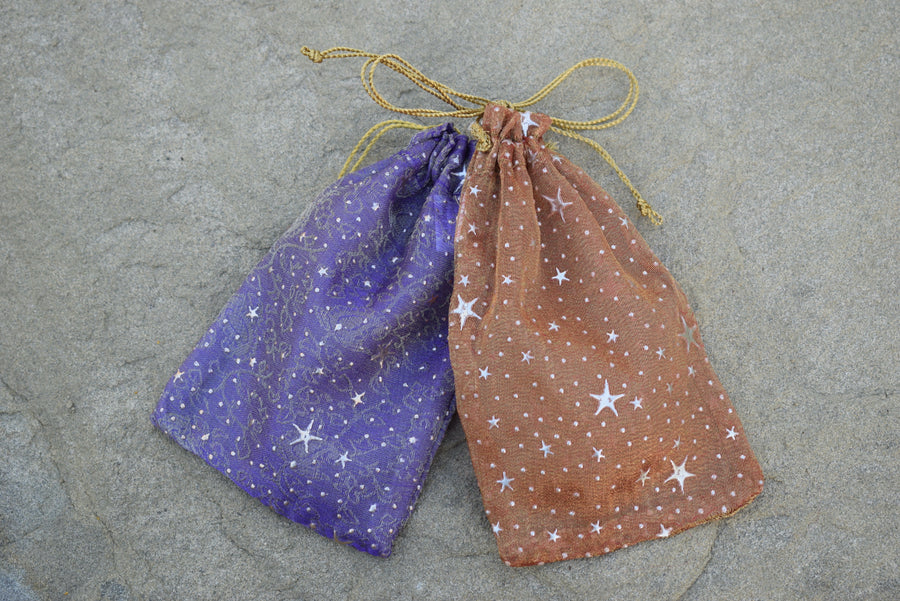 Two drawstring bags, a purple and a gold, resting on a rock