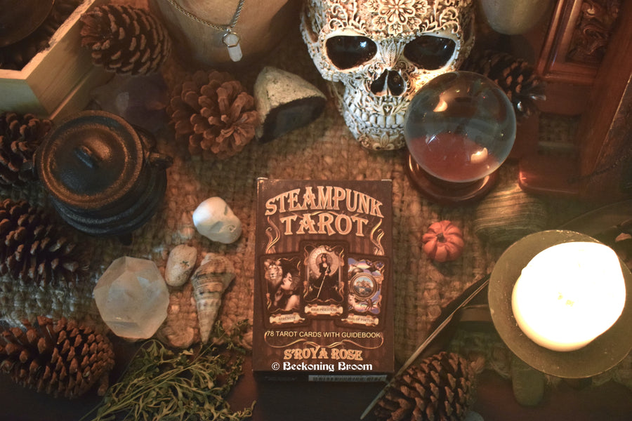 A tarot deck with Steampunk Tarot S'roya Rose written on the front rests on an altar with a skull, candle and other mysterious items.