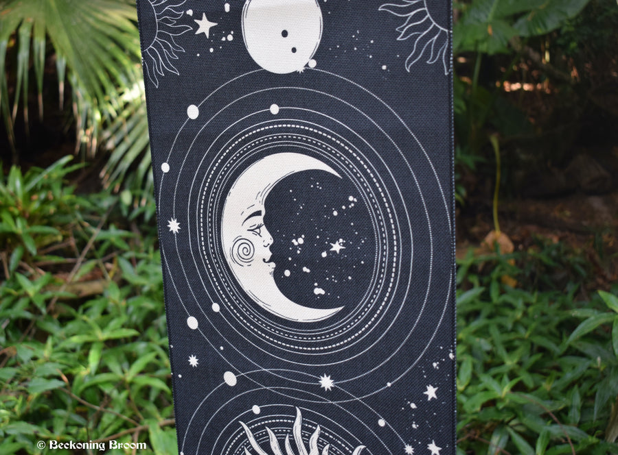 A detail of a black fabric tapestry depicting white moons with greenery in the background.