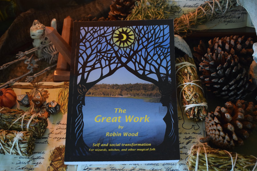 A book titled The Great Work by Robin Wood subtitled Self and social transformation for wizards, witches and other magical folk sitting on an altar with smudge sticks, pine comes, crystals and spells