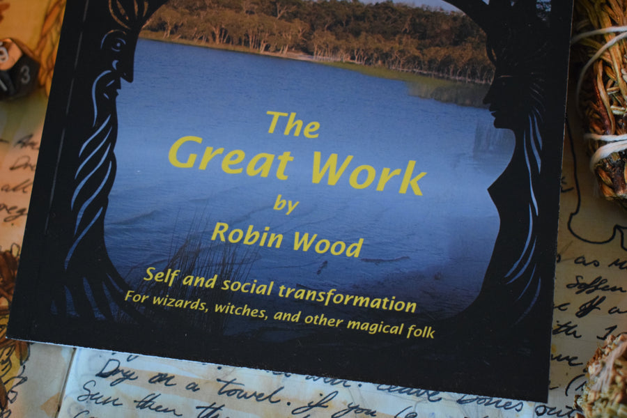 Bottom half of a book titled The Great Work by Robin Wood subtitled Self and social transformation for wizards, witches and other magical folk sitting on an altar with smudge sticks, pine comes, crystals and spells
