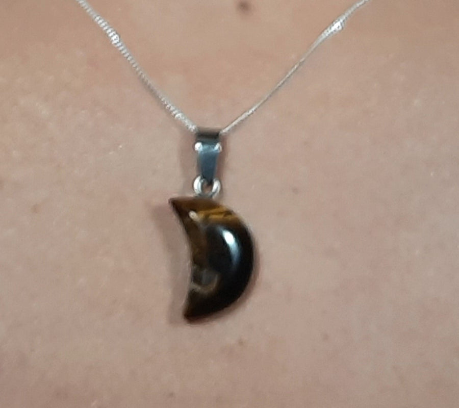 A tiger's eye crystal crescent moon necklace on a sterling silver chain hanging on the neck of a bronze person