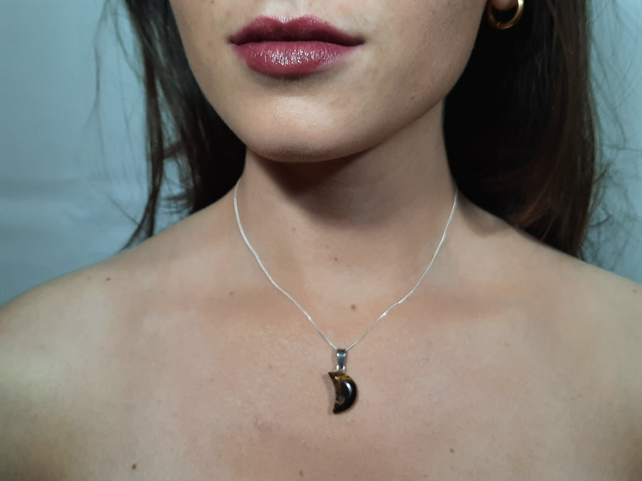 A tiger's eye crystal crescent moon necklace on a sterling silver chain hanging on the neck of a person