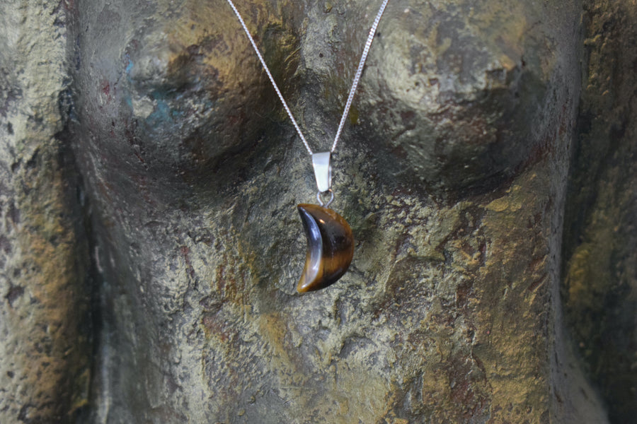 A tiger's eye crystal crescent moon necklace on a sterling silver chain hanging on the neck of a bronze goddess sculpture