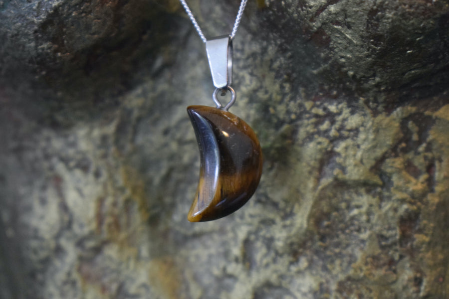 A tiger's eye crystal crescent moon necklace on a sterling silver chain hanging on the neck of a bronze sculpture