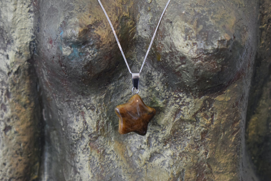 A tigers eye crystal crescent moon necklace on a sterling silver chain hanging on the neck of a bronze goddess sculpture