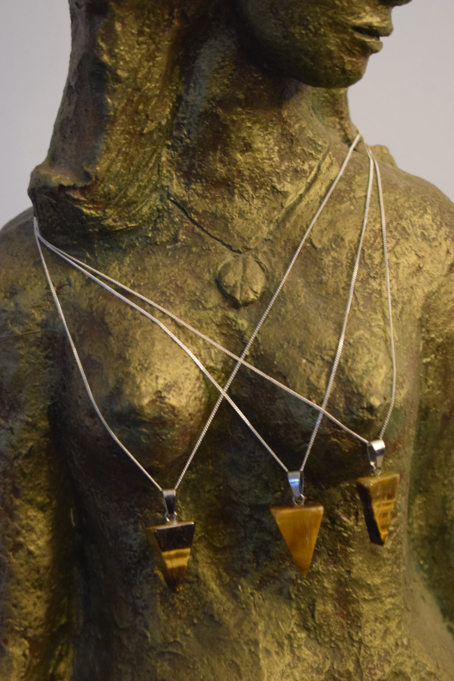 Bronze goddess sculpture wearing three tiger's eye triangle pendants on silver chains