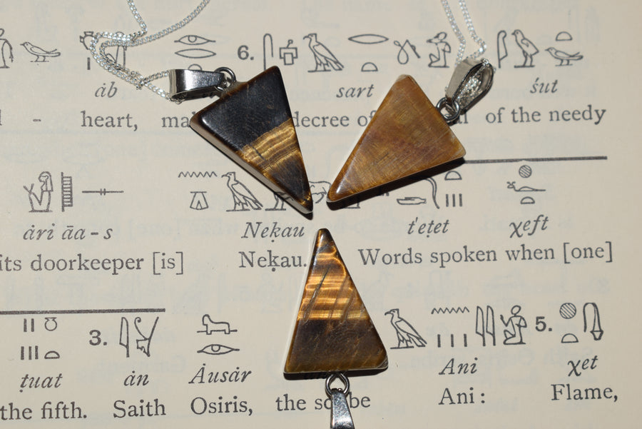 Three tiger's eye crystal triangle pendants on silver chains resting on egyptian hieroglyphic parchment